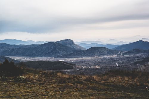 Free A beautiful view of hilly grasslands extending to distant mountains under a cloudy sky. Stock Photo