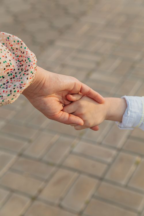 Free From above of anonymous mother and unrecognizable kid holding hands on street against blurred pavement in daylight in city outside Stock Photo