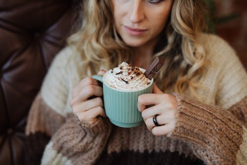 Woman in Brown Sweater Holding Green Ceramic Mug With Brown and White Liquid