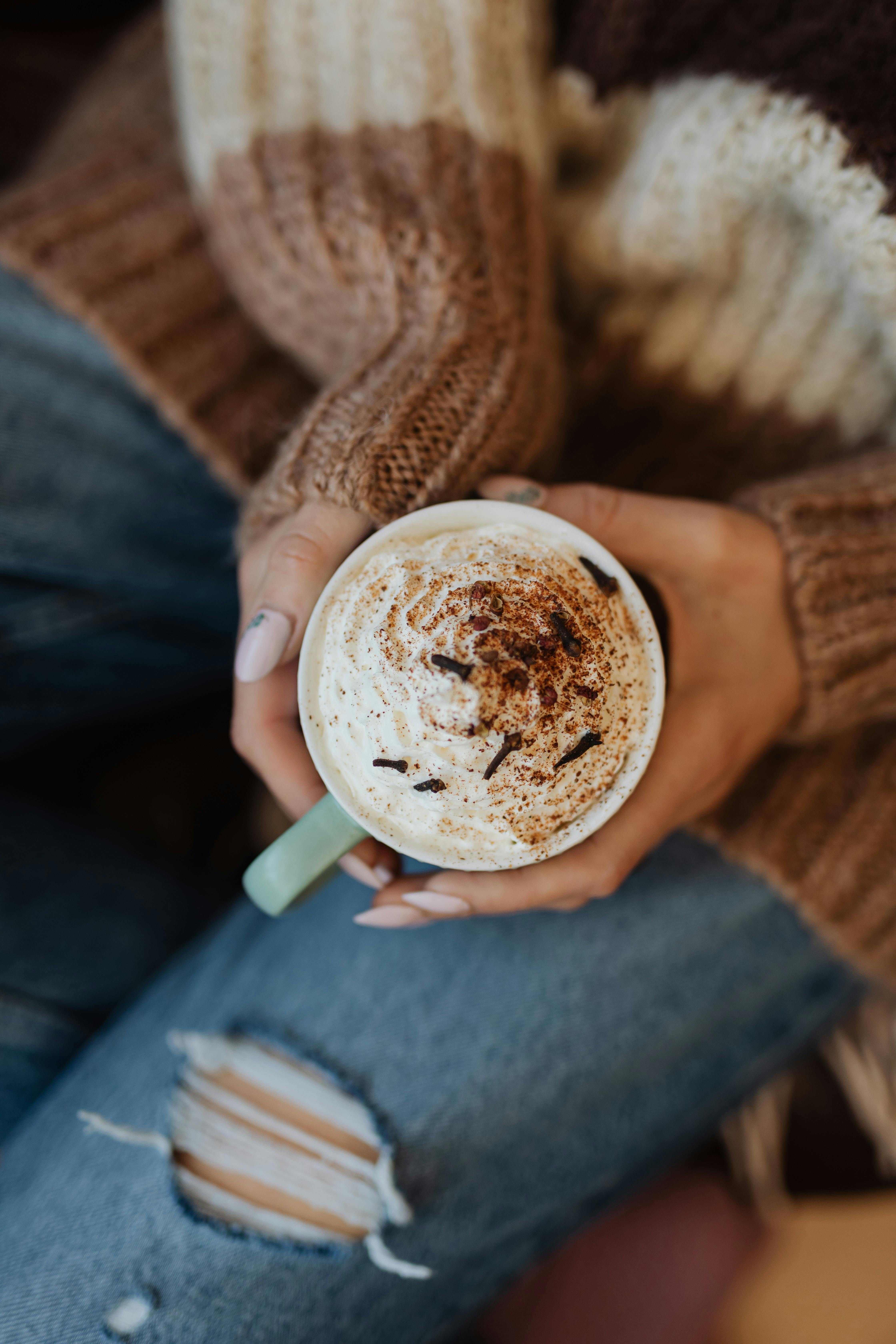 Enjoying a warm coffee with whipped cream while wearing a cozy sweater and ripped jeans.