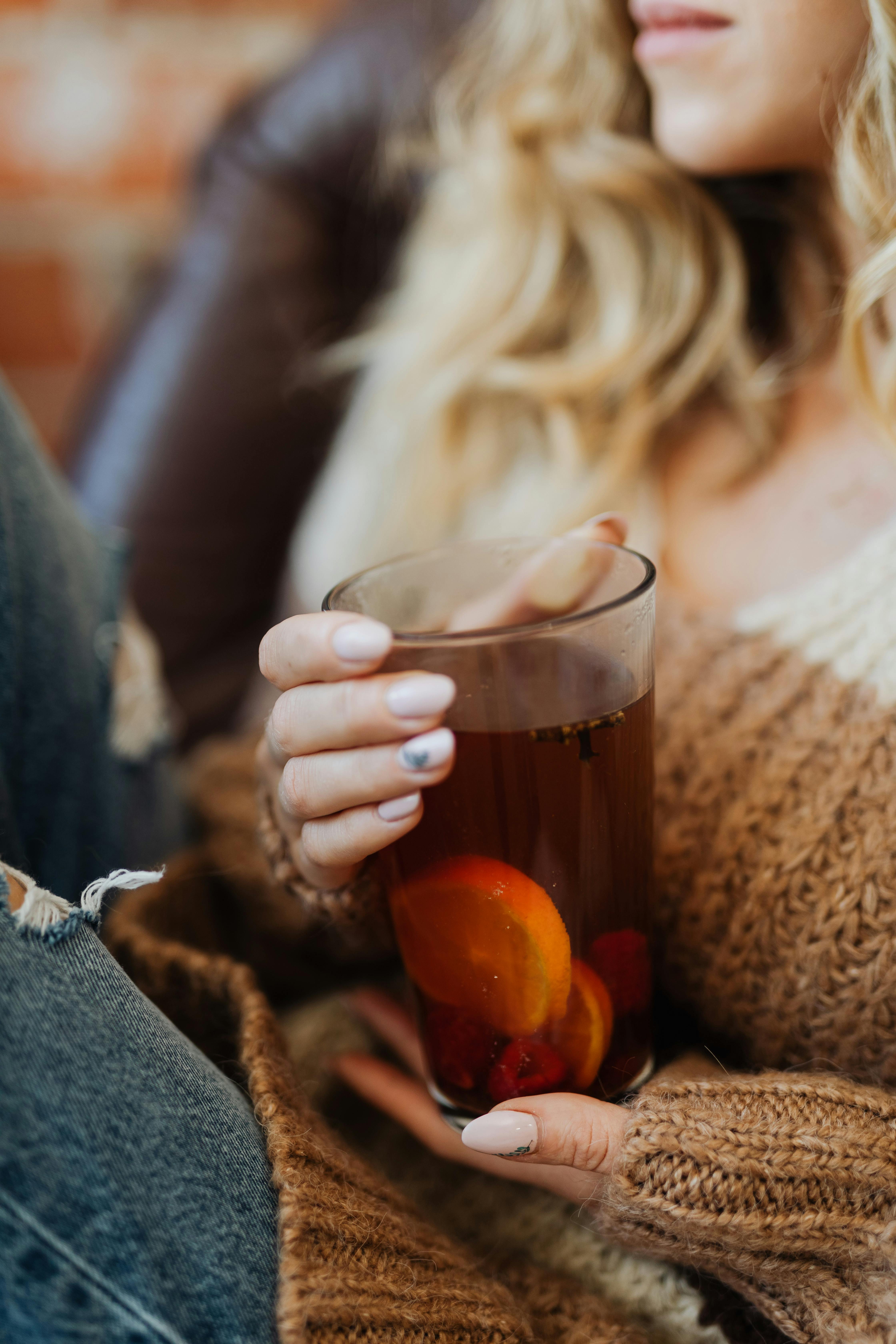 A woman enjoys a warm cup of tea with lemon and raspberries, embodying cozy autumn relaxation.
