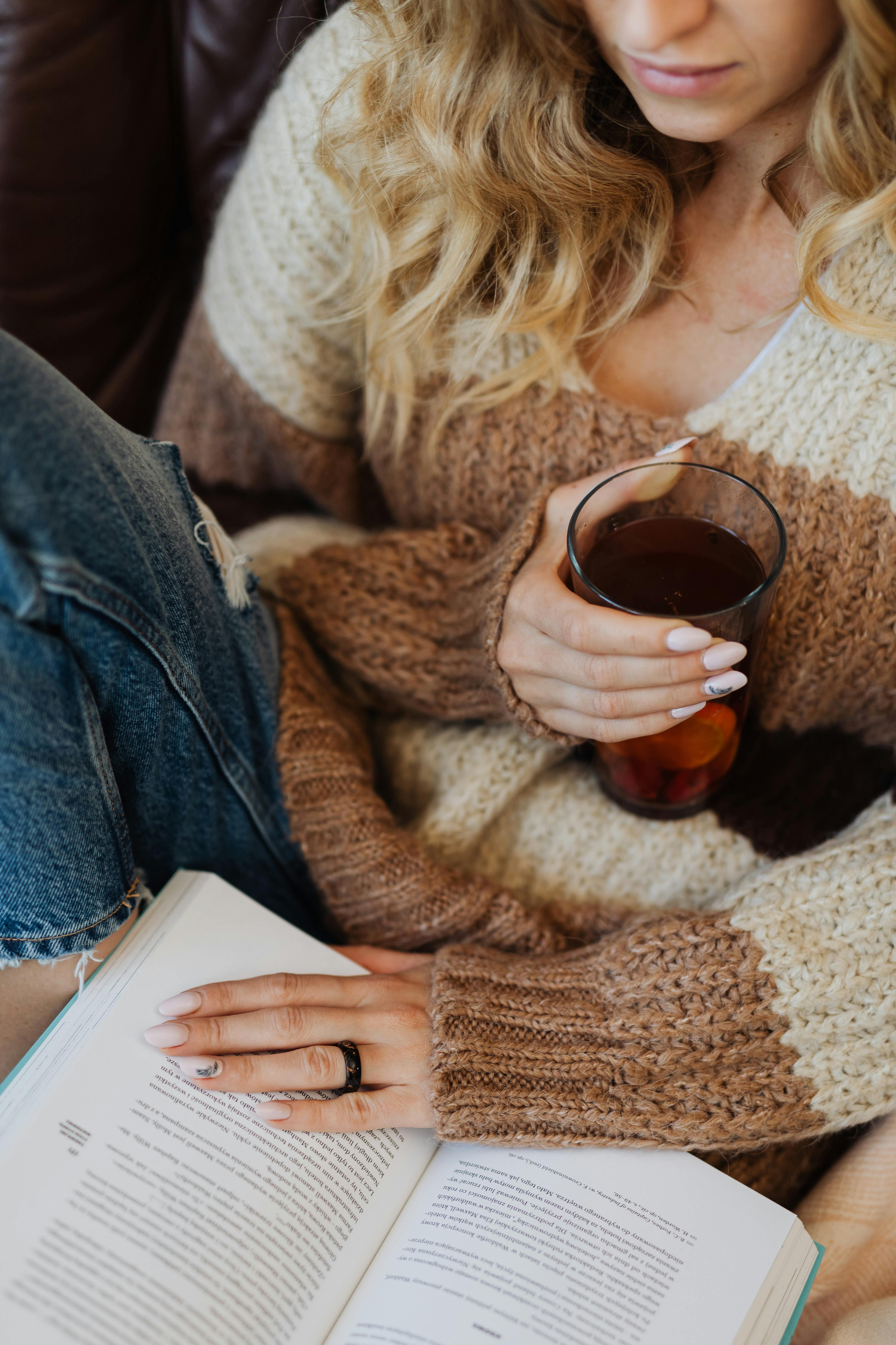 Woman enjoying a cozy moment reading a book with a cup of tea indoors.