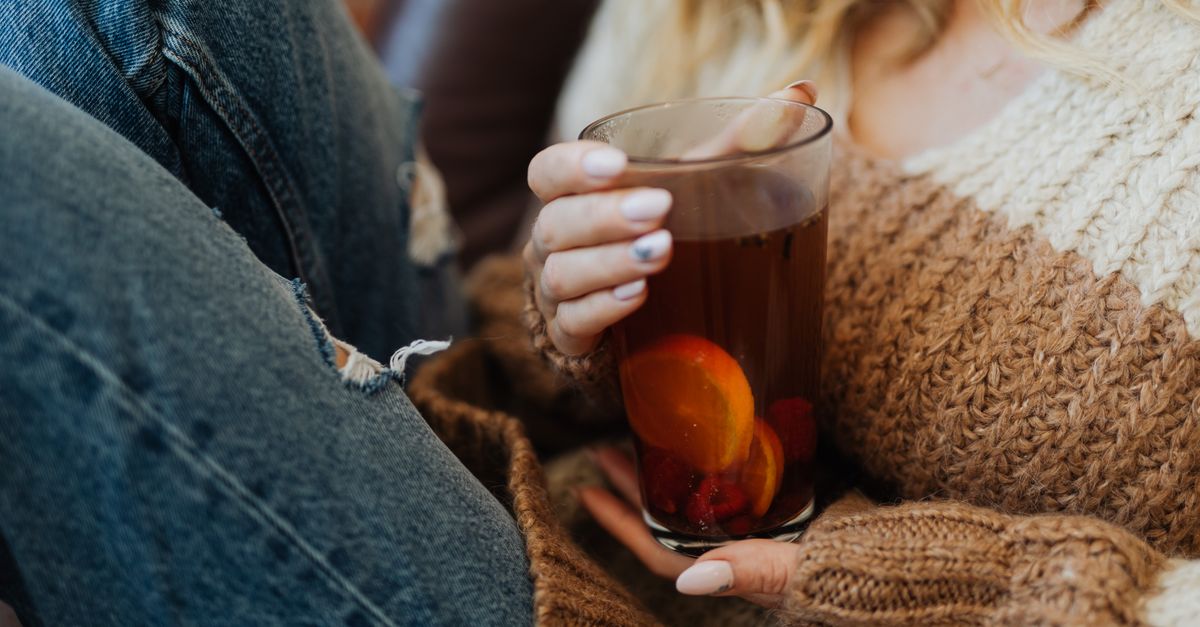 Woman in a sweater holding a glass of tea with lemon, evoking a cozy autumn vibe.