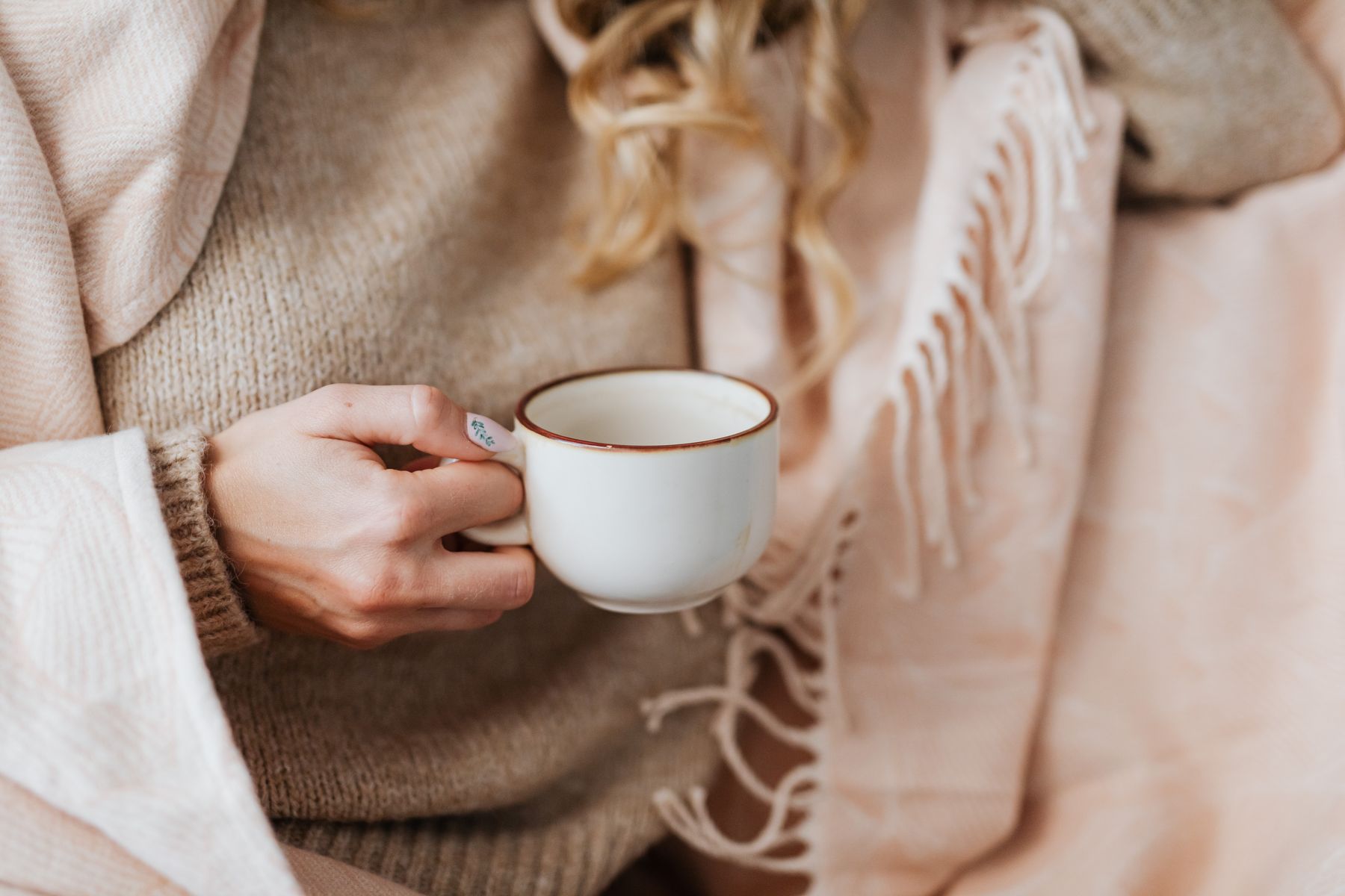 Close up of a woman's hands cradling a coffee cup, wrapped in a blanket