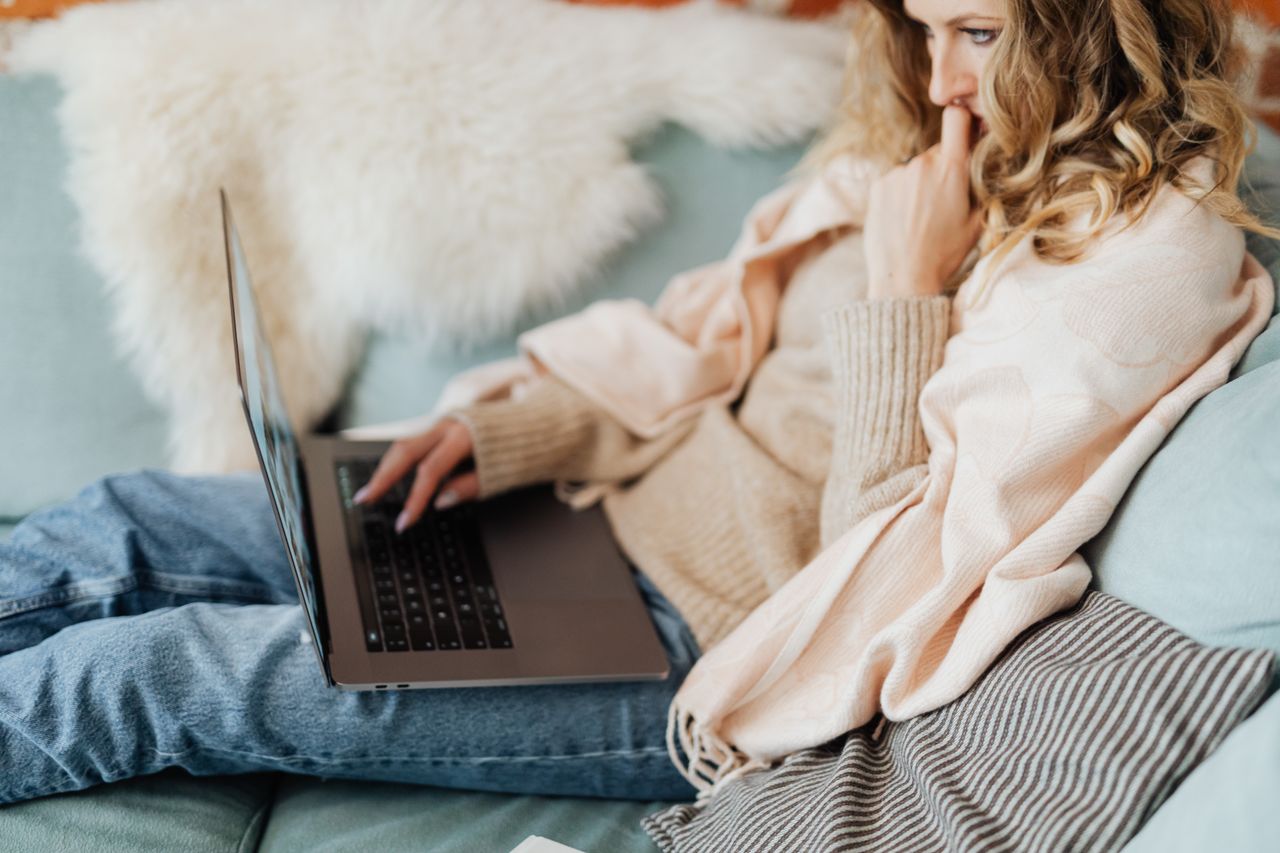 Woman relaxing on a couch with throw blankets and laptop