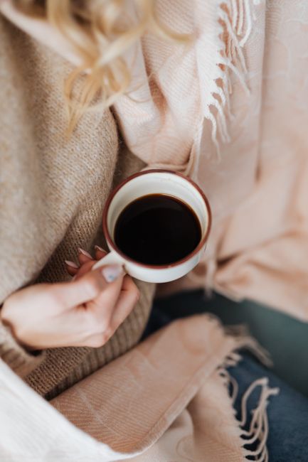 A person holding a warm cup of coffee, wrapped in cozy layers, providing a tranquil and warm atmosphere.