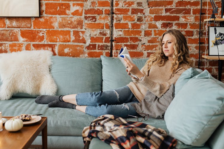 A Woman Reading A Book While Sitting On A Couch