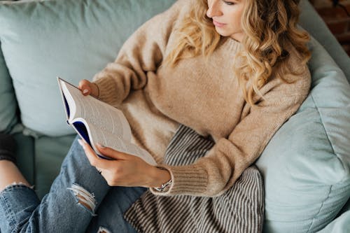 Free Woman in Knitted Sweater and Denim Jeans Reading a Book Stock Photo