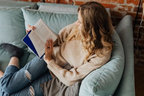 Free A woman enjoys a quiet moment reading on a cozy sofa indoors. Stock Photo