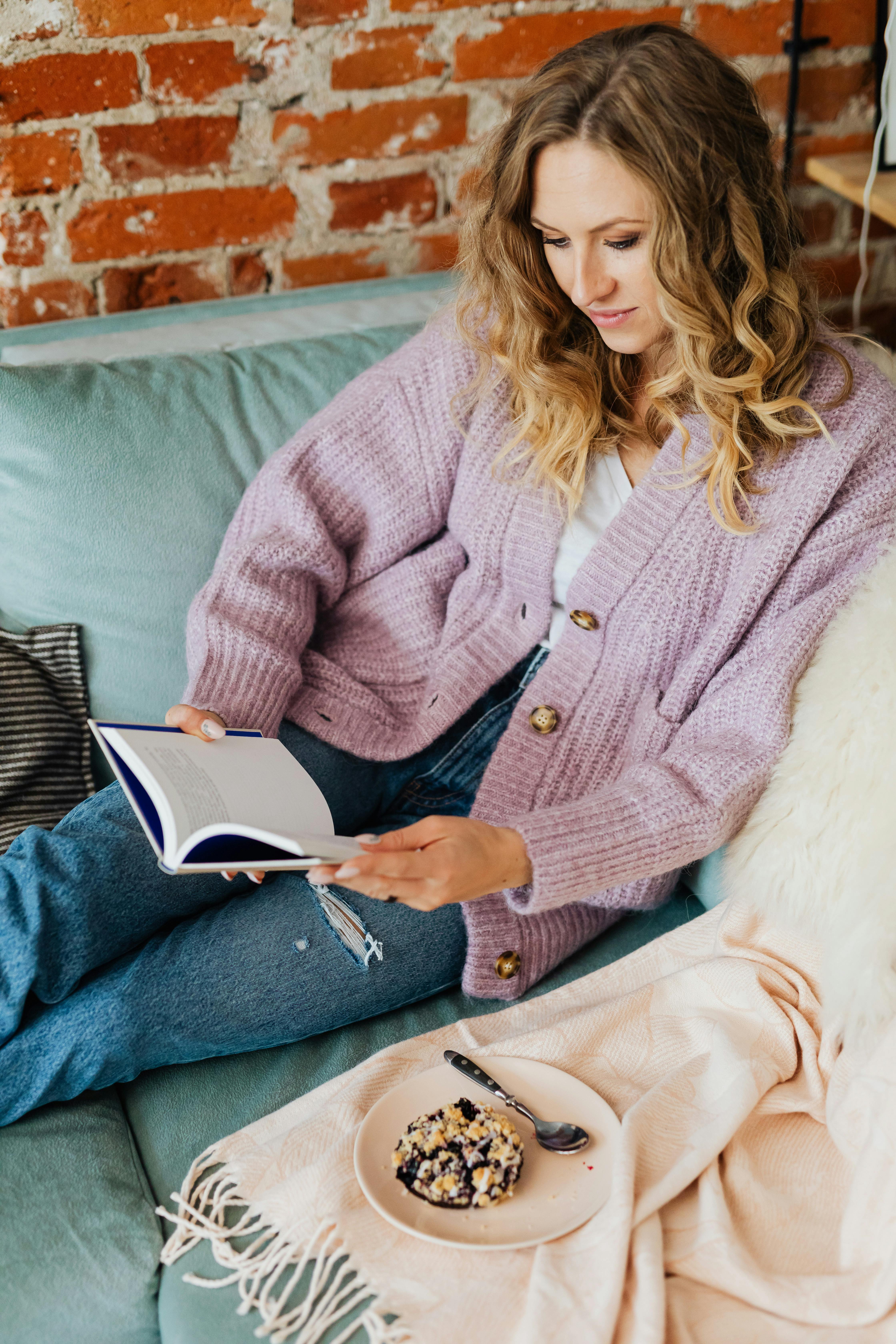 Free Young Woman with Book and Cake on Sofa Stock Photo