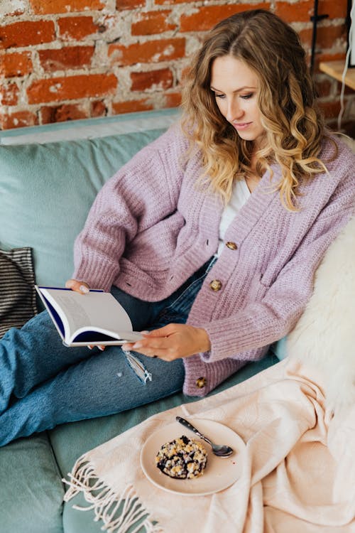 Young Woman with Book and Cake on Sofa