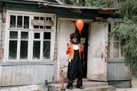 A Scary Man Holding a Red Balloon in Front of the Abandoned House