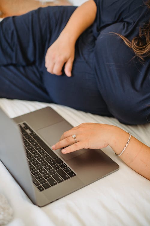 Crop expectant woman surfing internet on laptop in bedroom