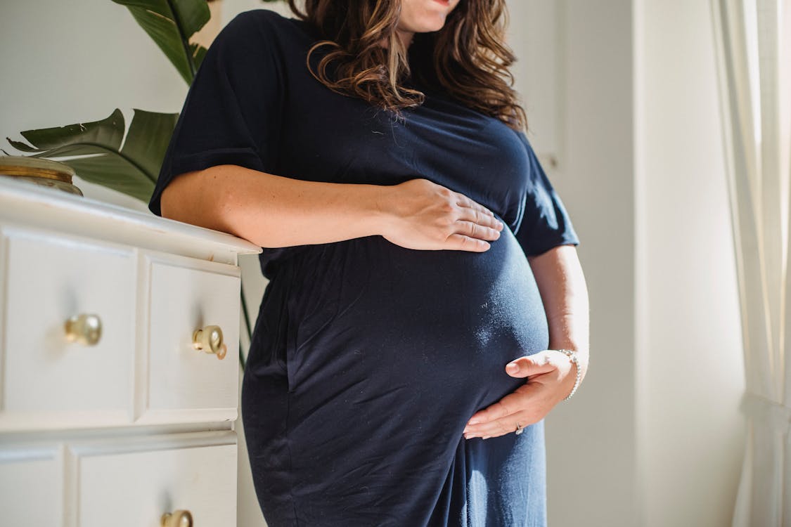Free Crop pregnant woman embracing tummy in room at home Stock Photo