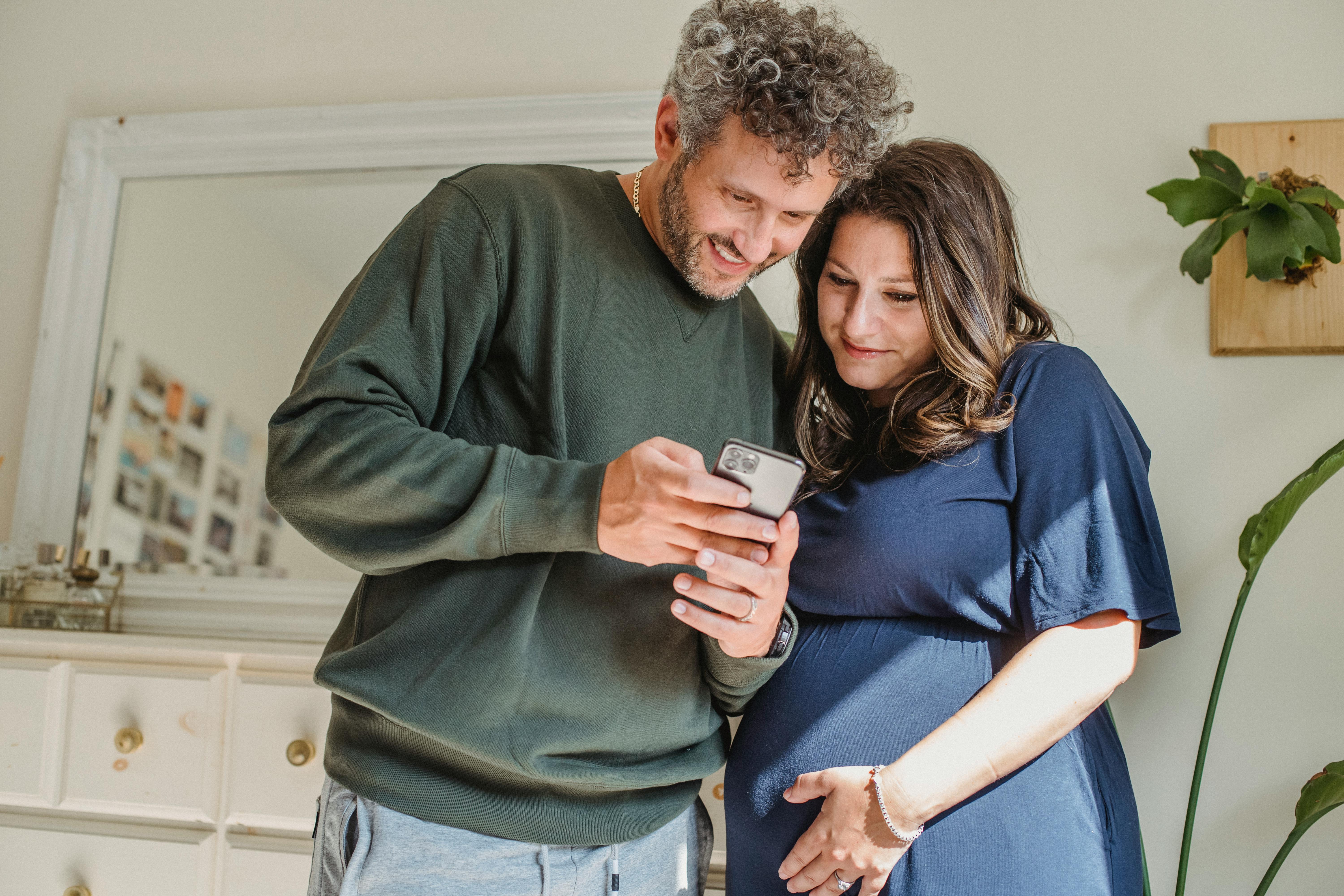 Pregnant woman and man watching smartphone together at home. | Photo: Pexels
