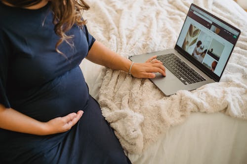 Free From above of crop anonymous expectant female caressing belly while surfing internet on netbook on cozy bed Stock Photo