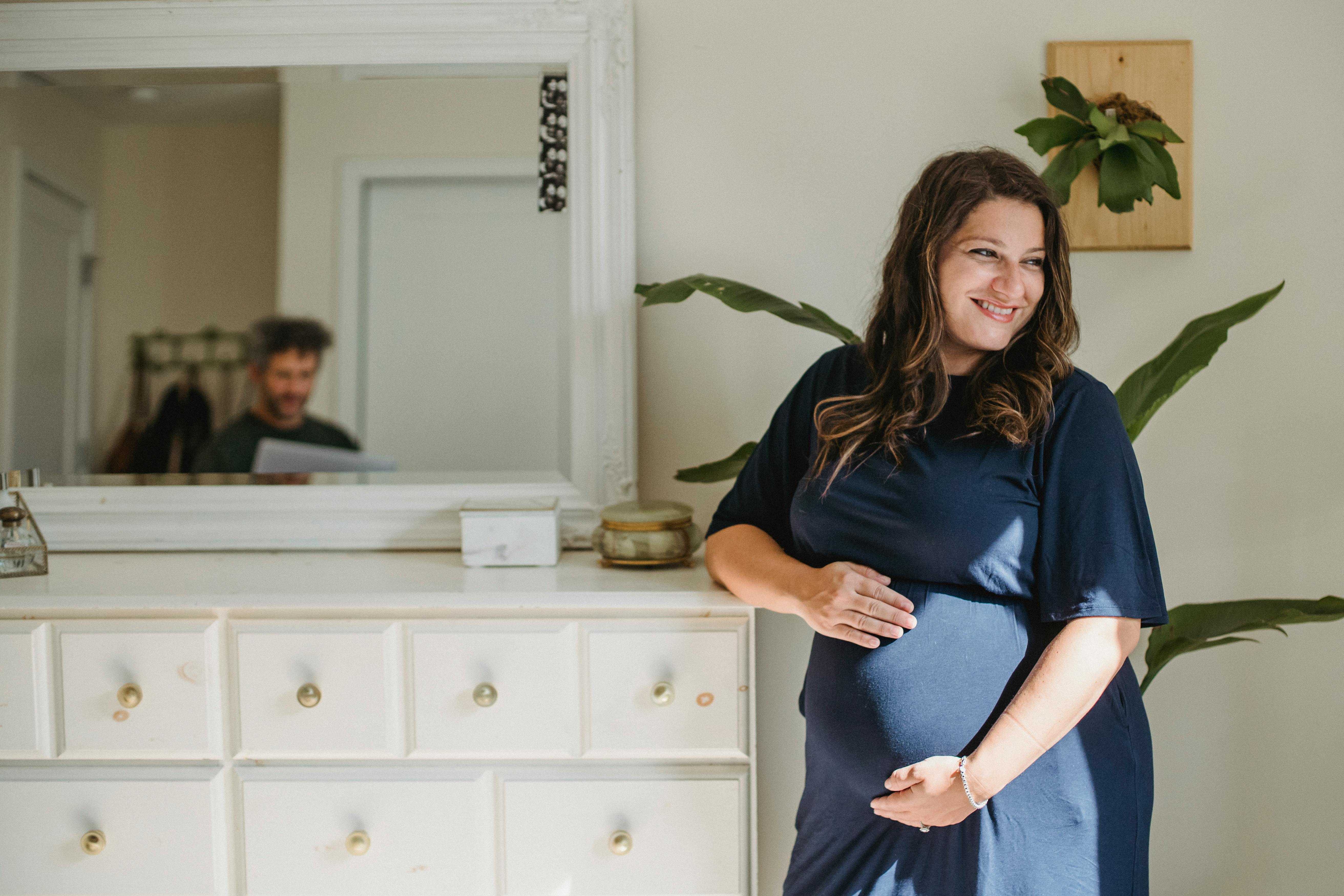 smiling pregnant woman and husband reflecting in mirror at home