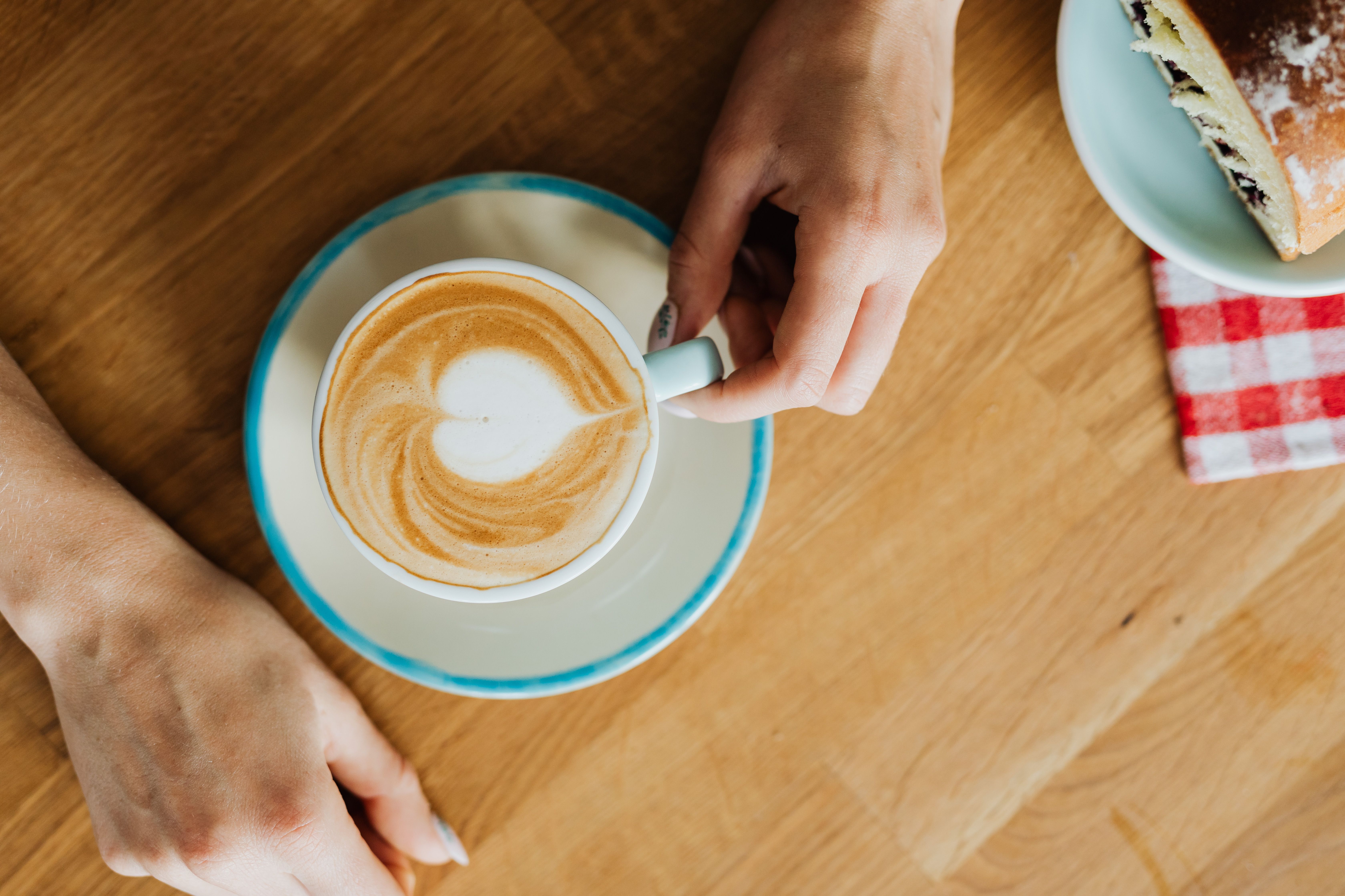 Top view of hands holding a latte with a pastry on a wooden table.