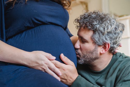 Free Bearded man kissing tummy of crop pregnant wife at home Stock Photo