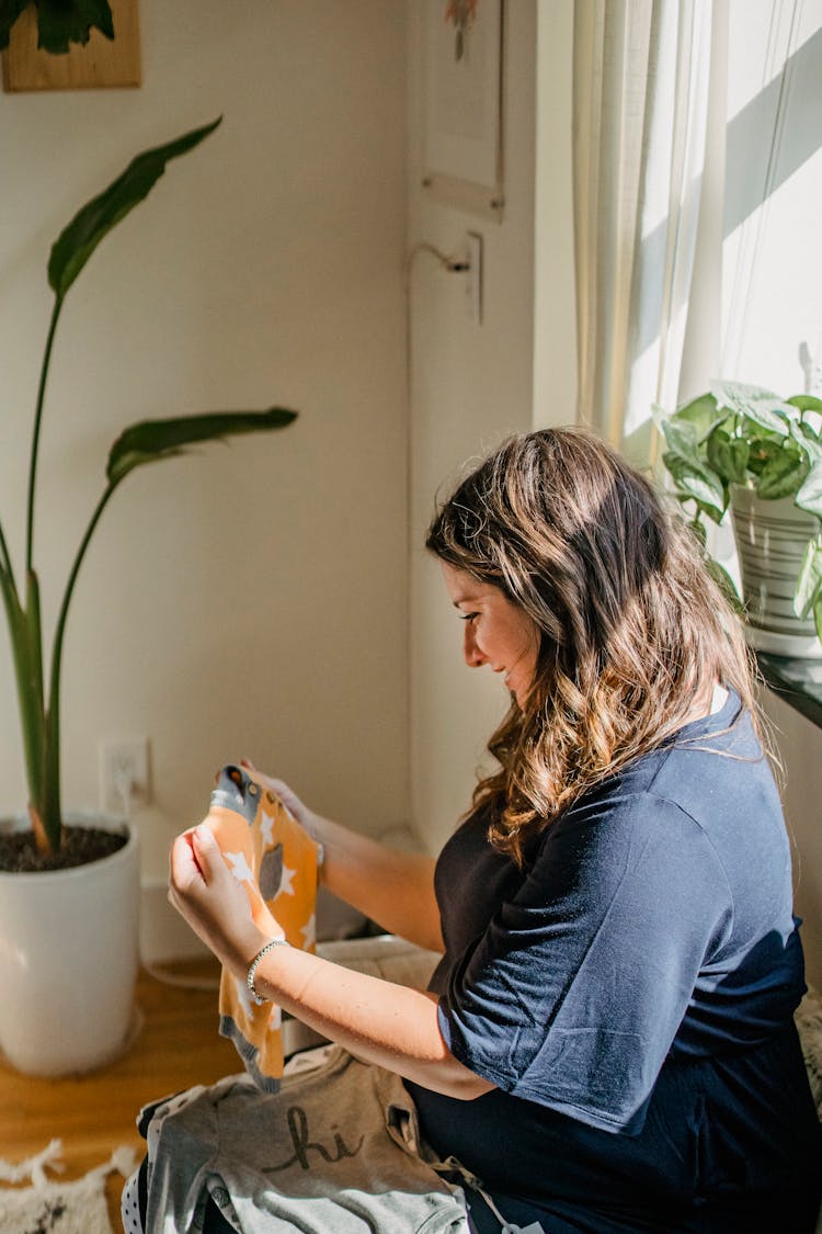 Happy Pregnant Woman Choosing Clothes For Baby