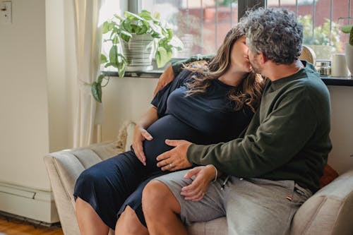 Couple expecting baby sitting on daybed and kissing