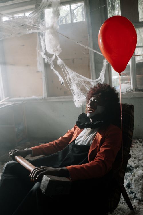 Free Eerie clown with red balloon in cobweb-filled abandoned building. Stock Photo