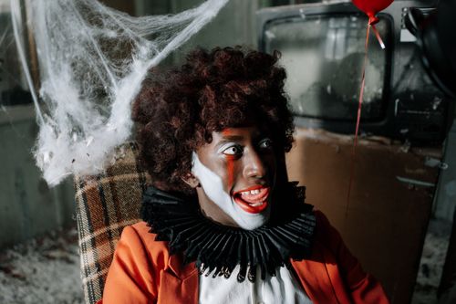 Free Dreadful clown with big smile and red balloon in eerie, cobweb-filled room. Stock Photo