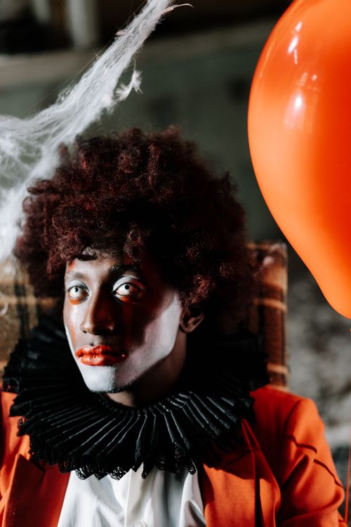 Free Eerie clown in costume with red balloon evokes Halloween horror vibe. Stock Photo