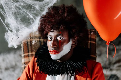 Free Spooky clown face with dramatic makeup, holding a red balloon amidst cobwebs. Halloween vibe. Stock Photo