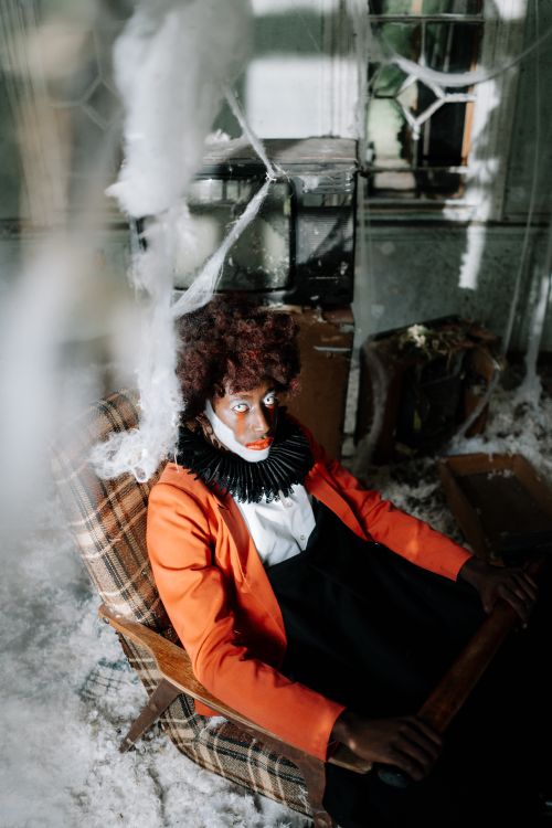 Free A costumed clown with makeup sits in an eerie, abandoned room filled with cobwebs and shadows. Perfect for Halloween themes. Stock Photo