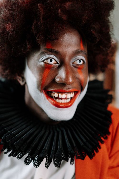 Free Close-up portrait of a creepy clown with eerie makeup, red nose, and a painted smile. Stock Photo