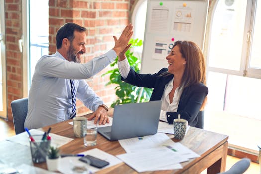 Two business professionals high-five in a modern office celebrating teamwork success.