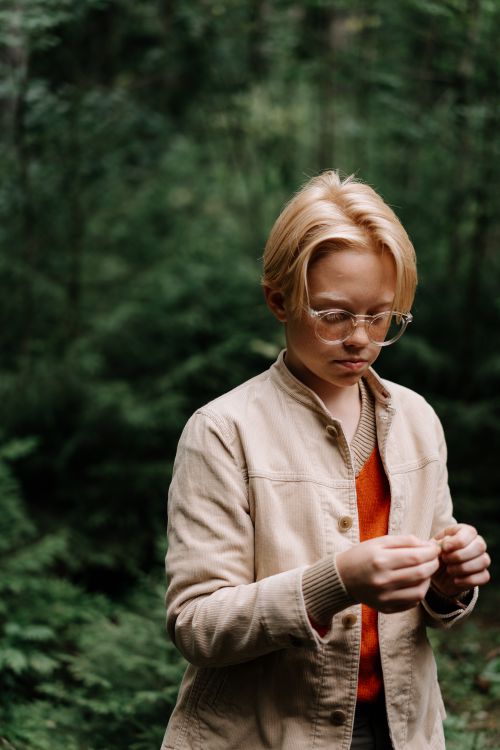 Free Teenager in glasses examines object in lush green forest with thoughtful expression, showcasing curiosity and nature exploration. Stock Photo