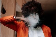 一个穿着橙色服装的阴险小丑在室内抽烟，营造出令人毛骨悚然的万圣节氛围