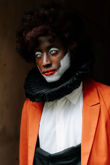 An eccentric portrait of a model with a painted face in fashion attire.