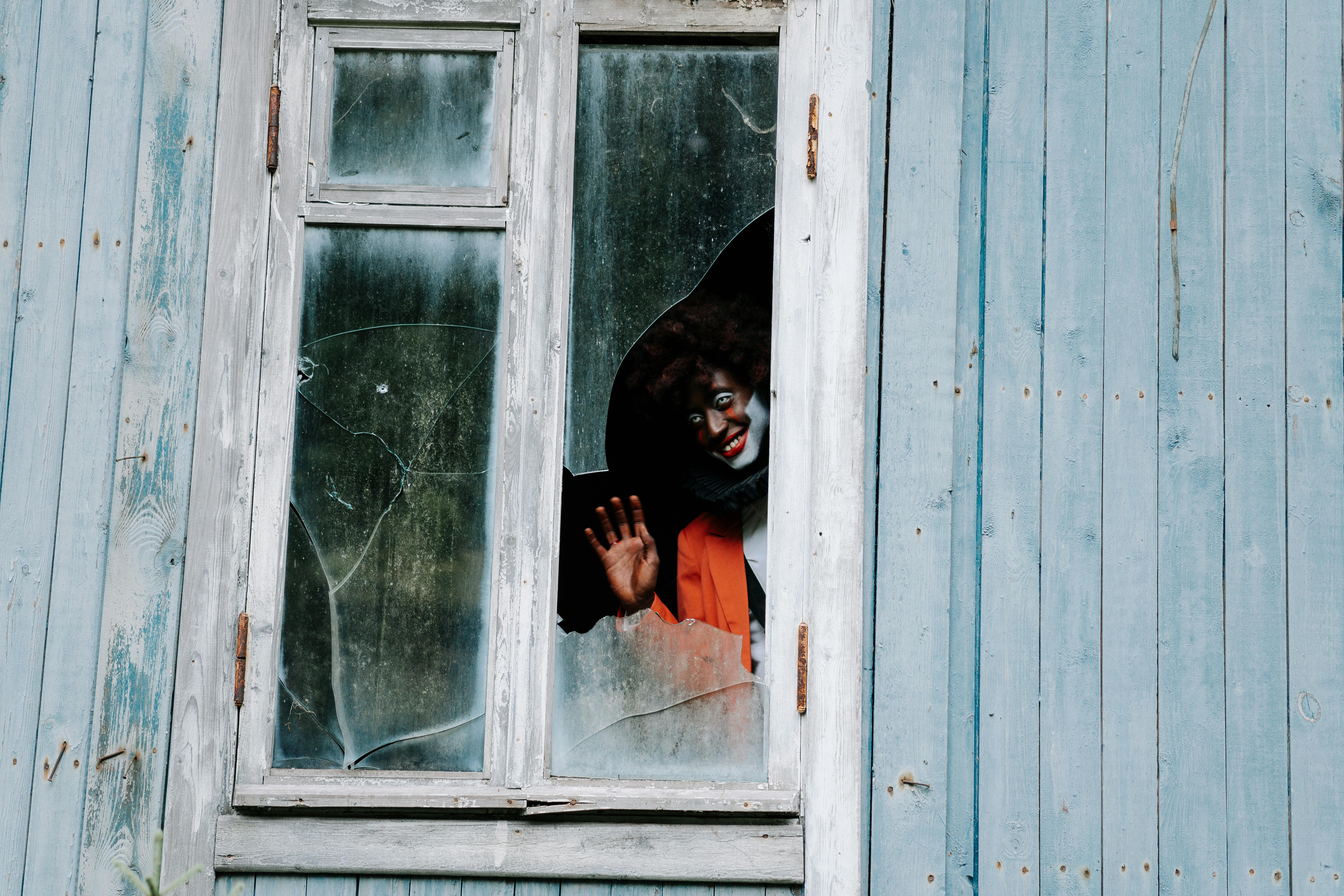 sinister clown waving on a shattered window