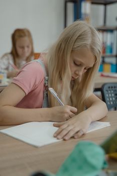 Blonde girl attentively taking notes in a classroom setting, conveying concentration and learning.