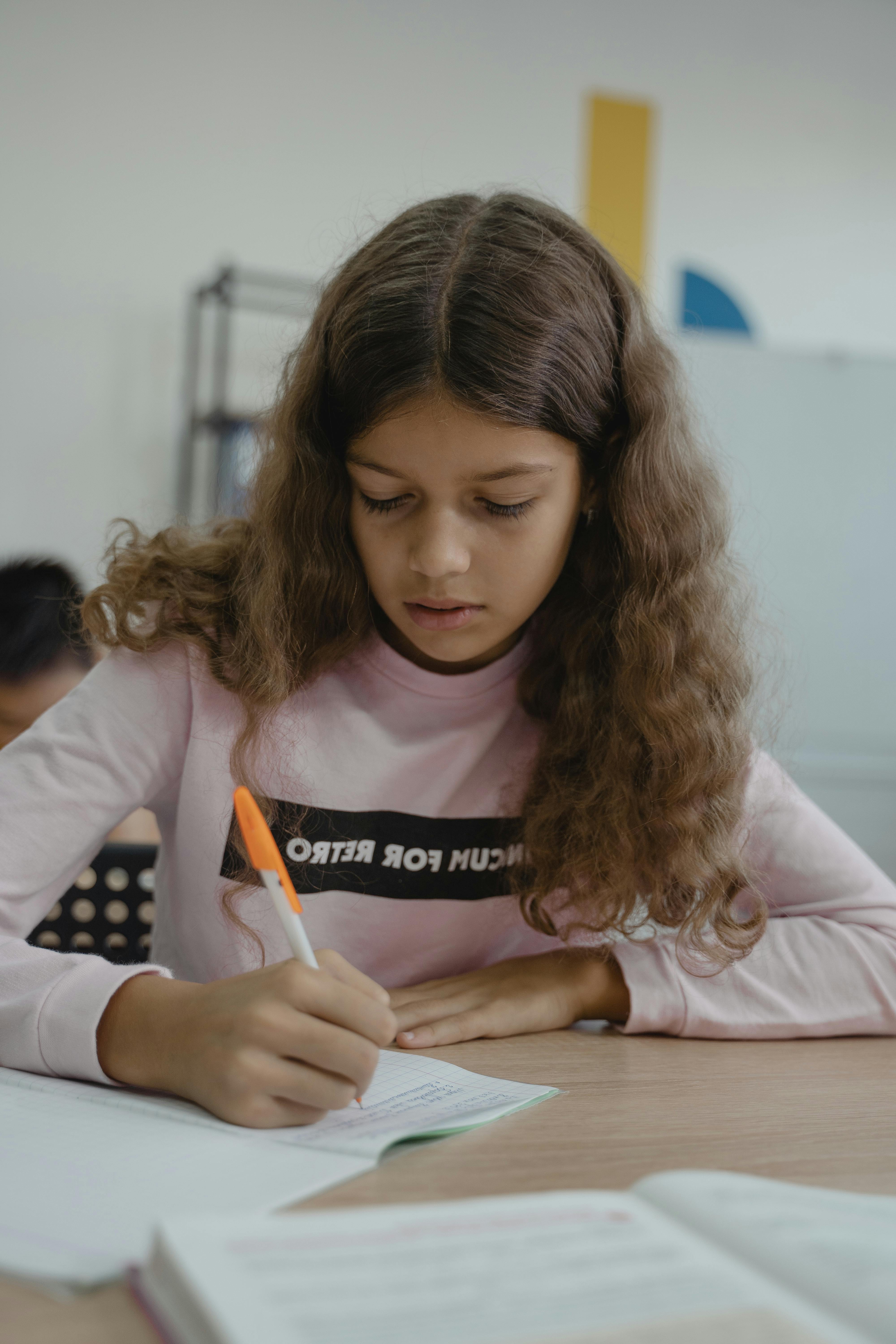 girl in pink long sleeve shirt writing on a notebook