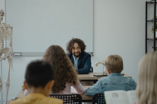Free Teacher explains human anatomy using a skeleton model in an interactive classroom setting. Stock Photo