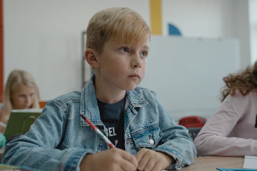 A young boy in a denim jacket attentively learning in a classroom setting.