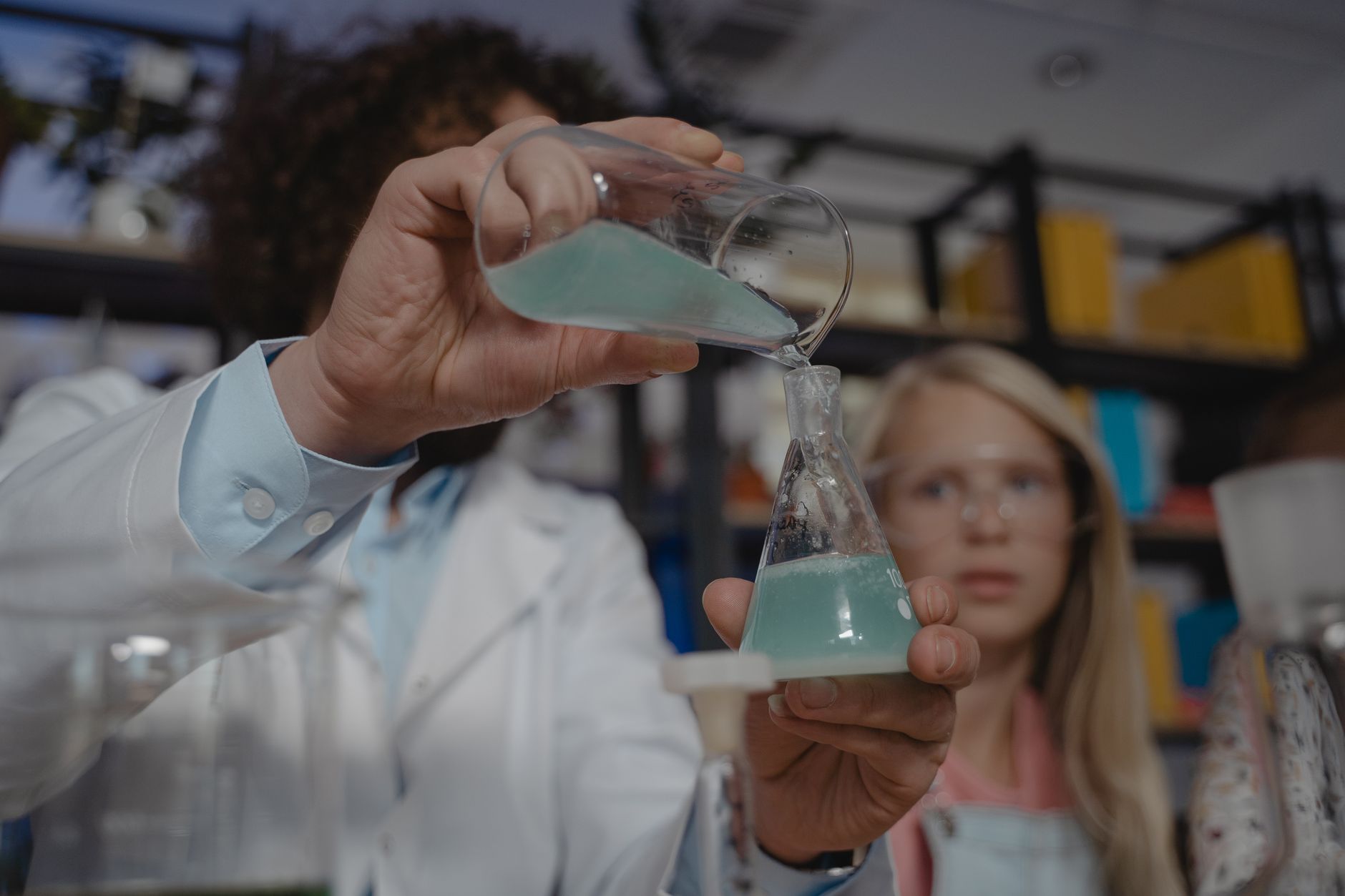 A student watches a teacher pour chemicals in a chemistry class experiment.