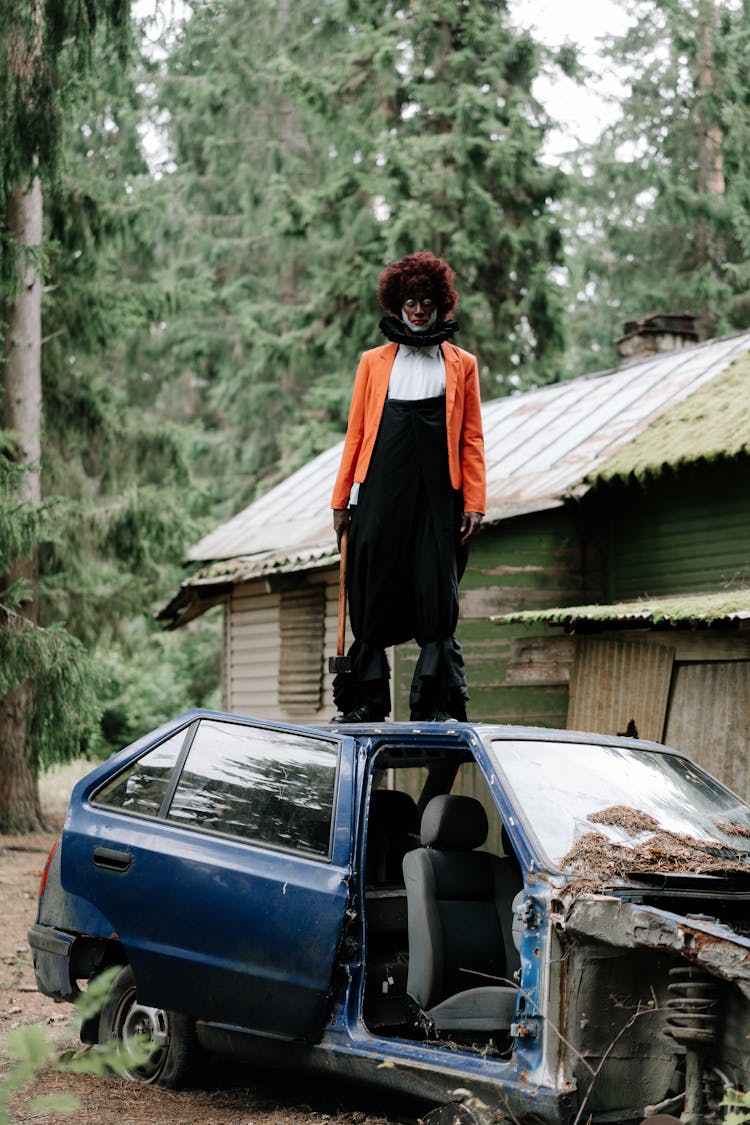 Scary Clown Holding A Sledge Hammer Standing On Top Of A Broken Car