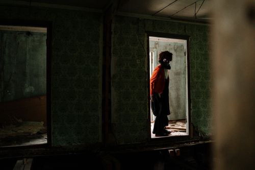 Free A mysterious figure dressed as a clown stands in the doorway of an abandoned building. Stock Photo