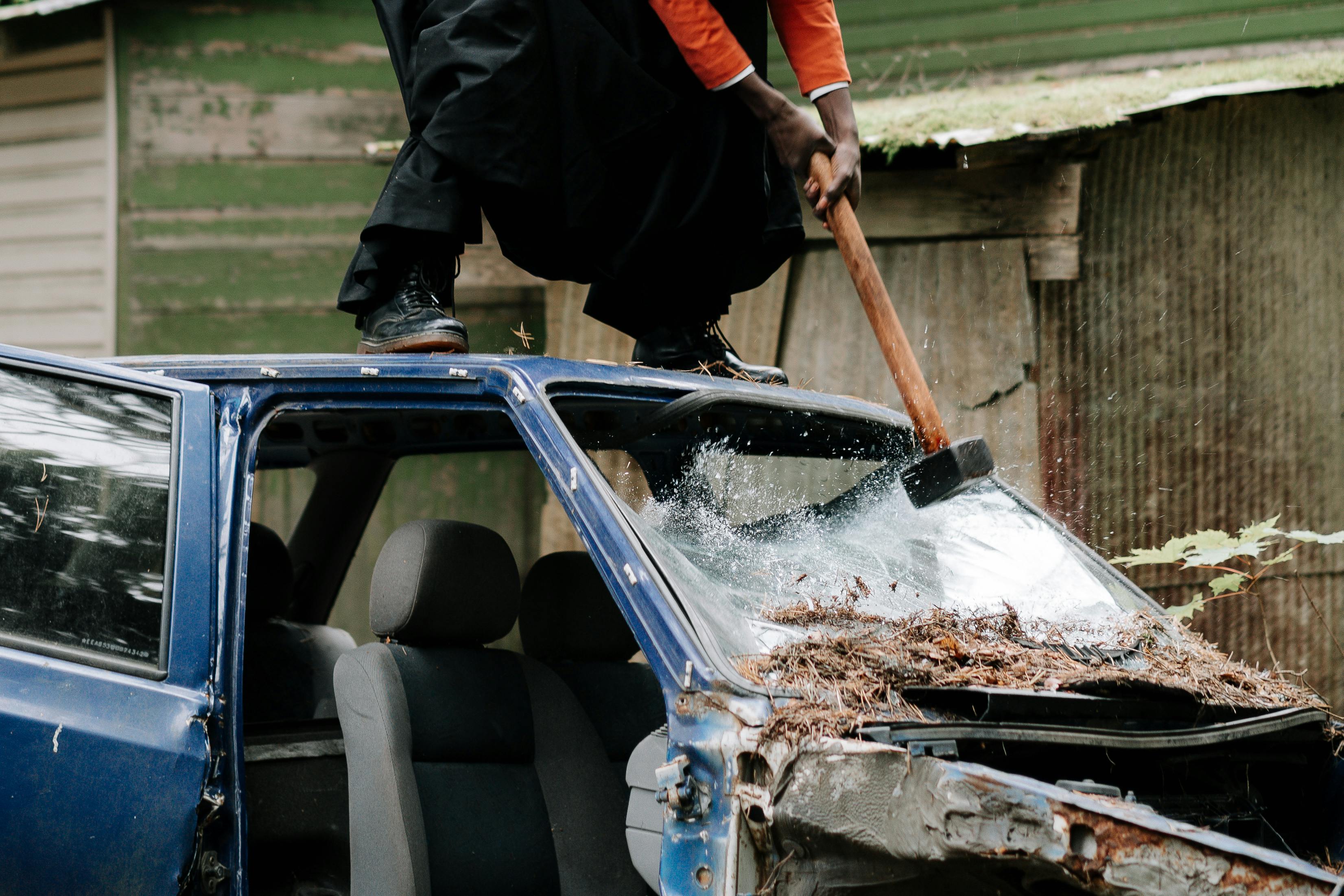 person smashing car windshield with a sledge hammer