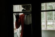 Man in White Dress Shirt and Red Vest Standing by the Window