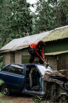 森林中，一个人拿着大锤撞上了一辆旧车，营造出一种诡异的氛围