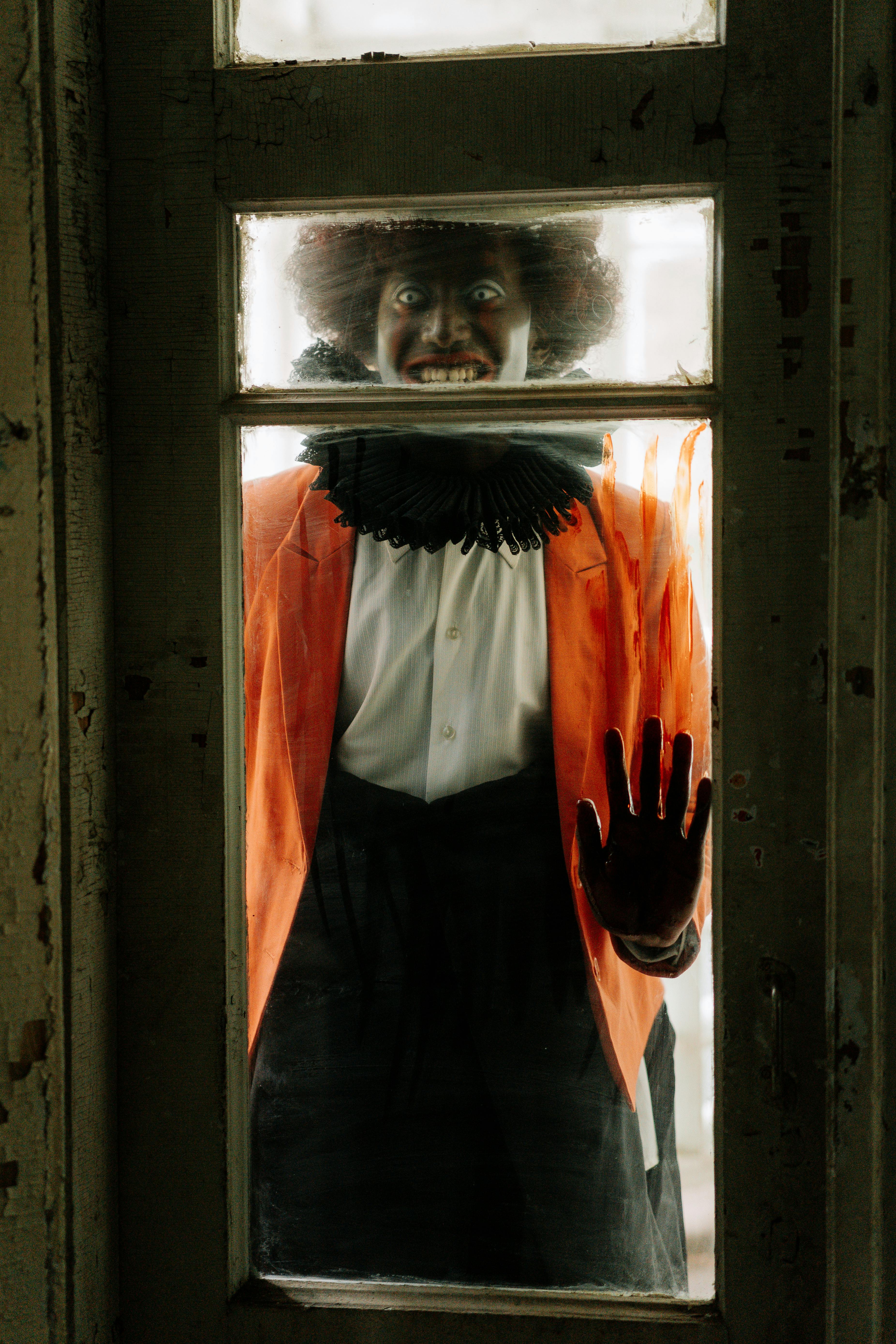 evil clown with bloody hand standing behind a glass door