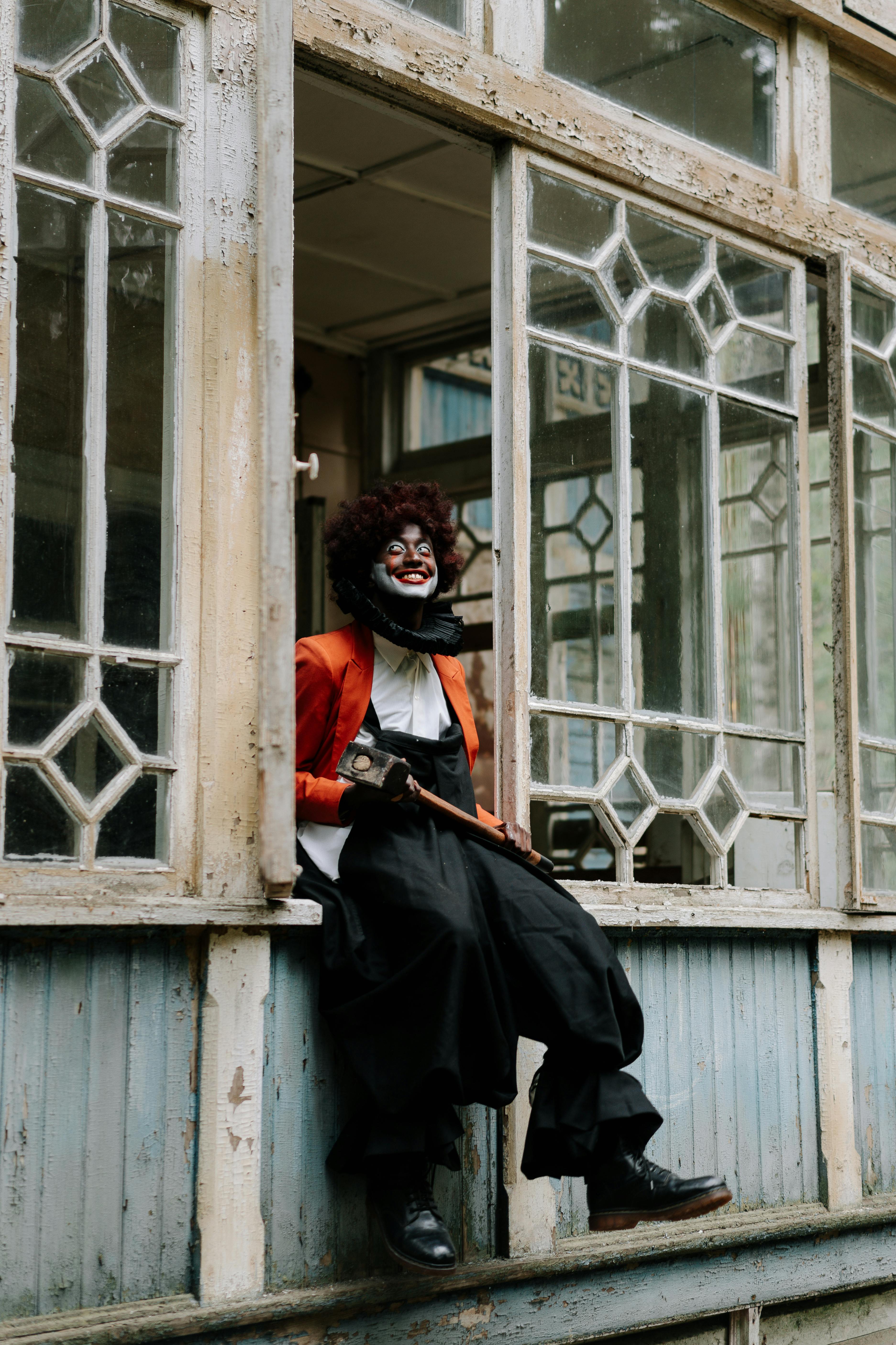 evil clown holding a sledge hammer sitting on window