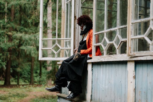 一名小丑穿着令人毛骨悚然的服装，坐在一栋被森林包围的废弃建筑的壁架上