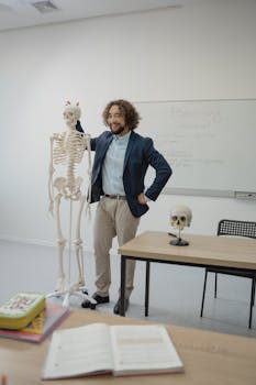 A smiling teacher stands beside a skeleton model in a biology classroom setting.